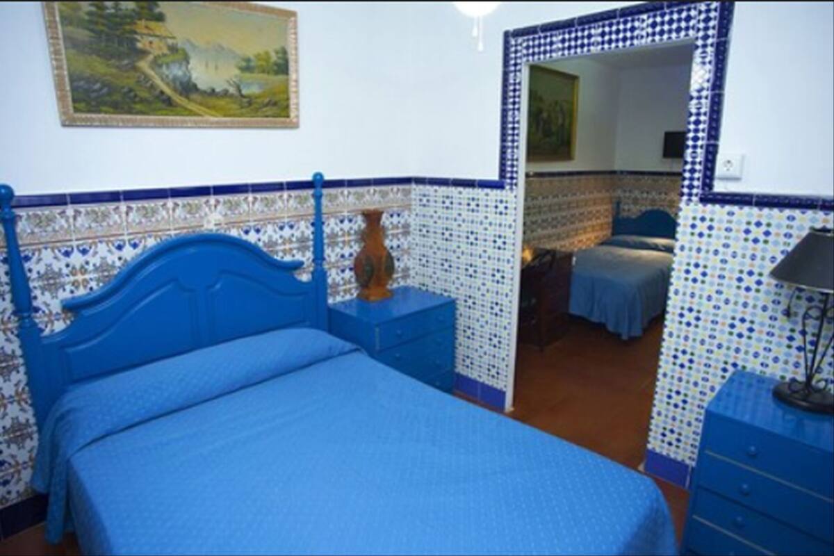 A bedroom with a blue bed, a dresser, a nightstand, and a mirror.