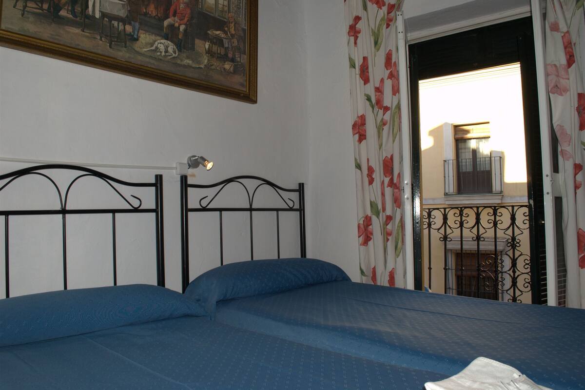 A bedroom with a bed, a painting on the wall, and a view of the outside through an open door.
