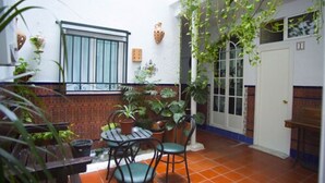 Un patio con una mesa y sillas, rodeado de plantas en macetas y un piso de baldosas.
