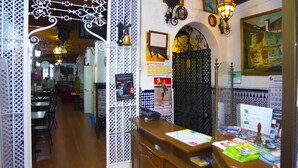 Interior de restaurante con un mostrador de recepción de madera, barandillas metálicas decorativas y una pared de azulejos con un cuadro.