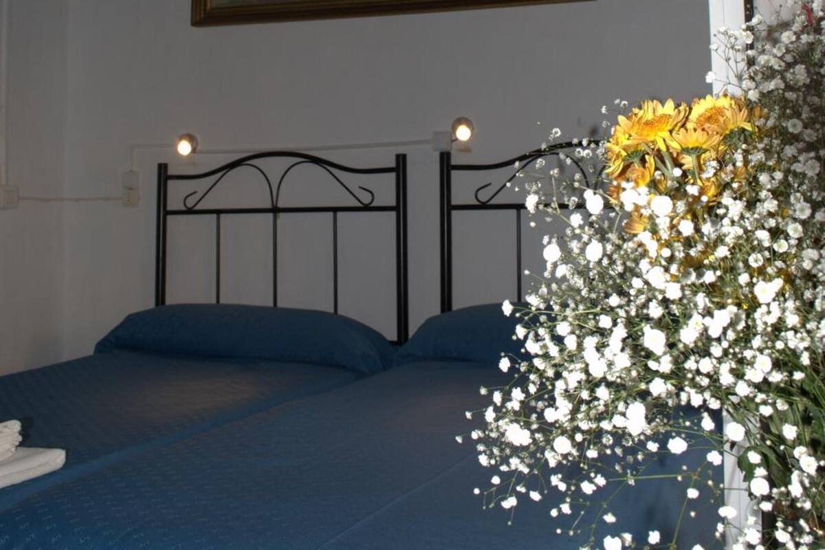 A bedroom with a bed, a painting on the wall, and a floral arrangement.