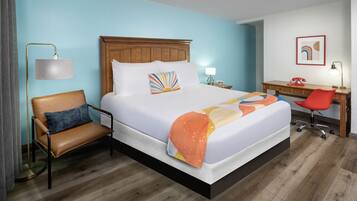A hotel room with a large bed, a desk, a chair, and a lamp.