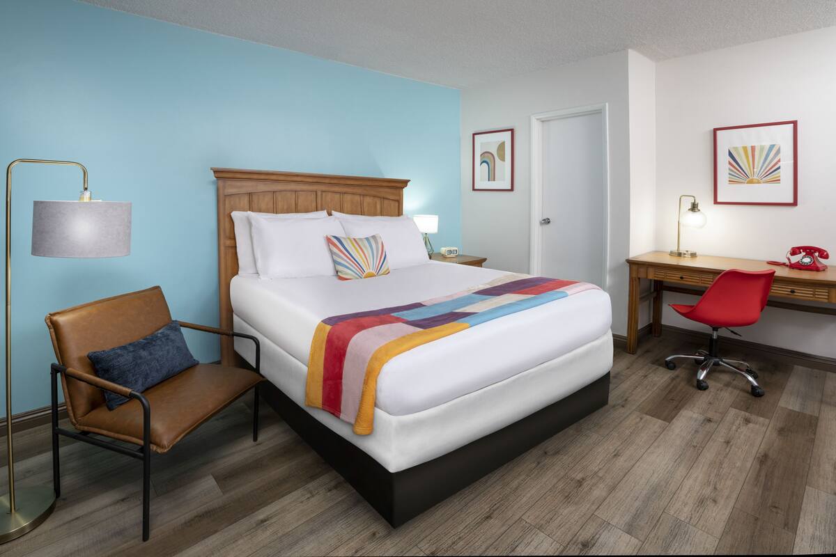 Ein Hotelzimmer mit Bett, Schreibtisch, Stuhl, Lampe und Bildern an den Wänden.