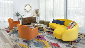 A living room with a yellow sofa, orange chairs, a round coffee table, and a patterned rug. - The Sojourn Los Angeles - Sherman Oaks (Sherman Oaks)