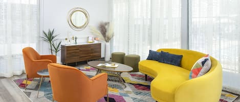 A living room with a yellow sofa, orange chairs, a round coffee table, and a patterned rug.