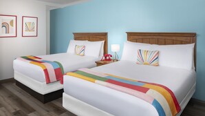 A hotel room with two beds, each with a colorful striped blanket and matching pillows. There is a nightstand with a red telephone and a lamp. The walls are painted light blue, and there are two framed pictures on the wall. - The Sojourn Los Angeles - Sherman Oaks (Sherman Oaks)
