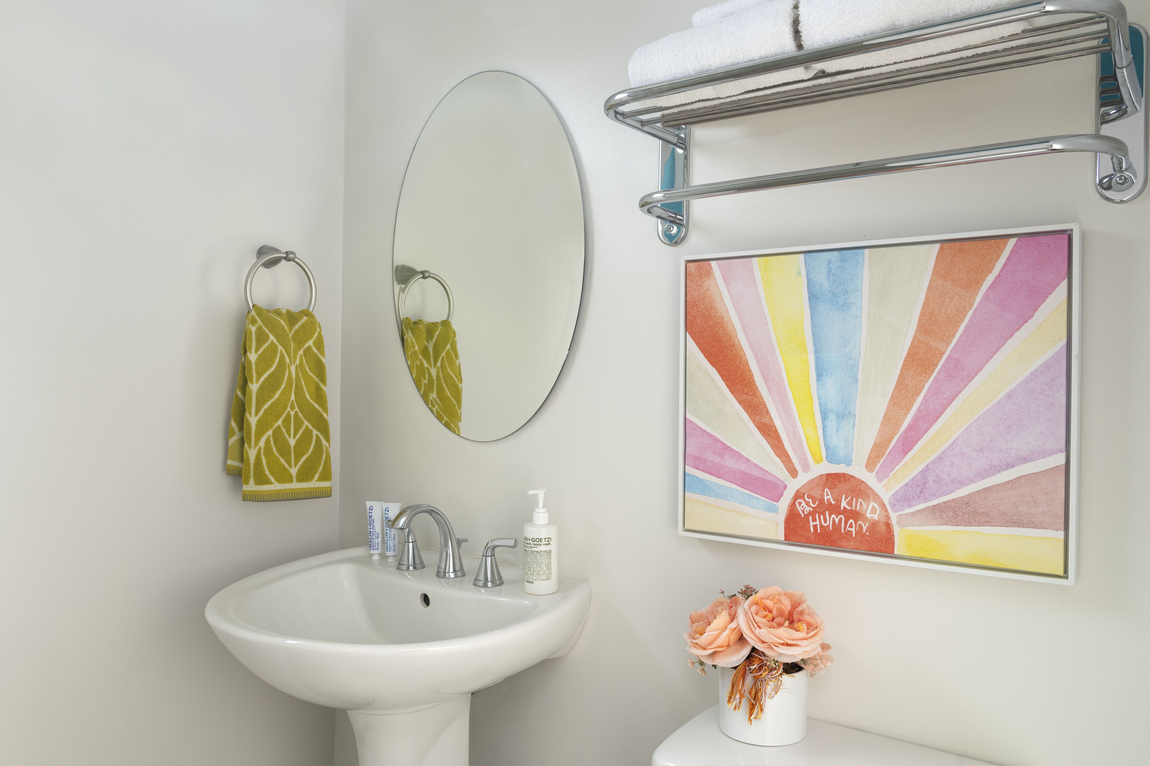 A bathroom with a white sink, a mirror, a towel rack, and a framed artwork.