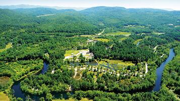 An aerial view of a park with a river, pathways, and scattered buildings.