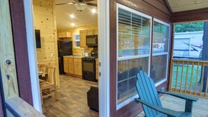 A wooden interior with a kitchen, a dining area, and a porch with a chair.