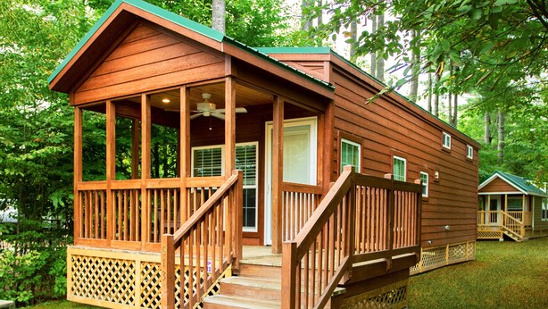A wooden cabin with a porch and a deck, surrounded by trees.