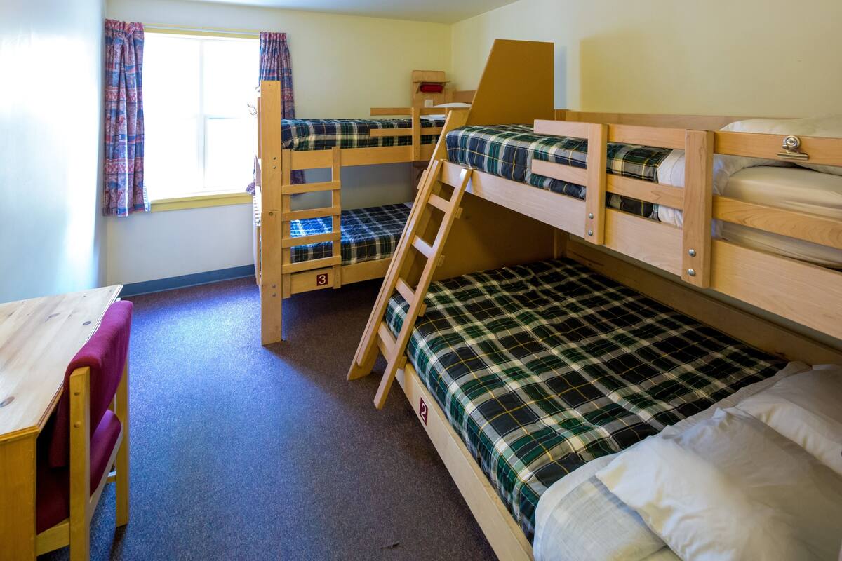 Une chambre avec un lit superposé, un bureau en bois et une fenêtre avec des rideaux.