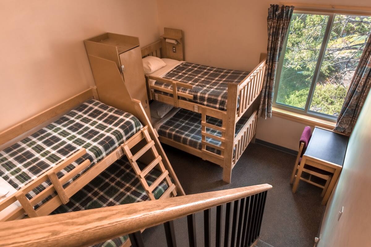 Une chambre de dortoir avec deux lits superposés, une petite table et une fenêtre donnant sur les arbres.