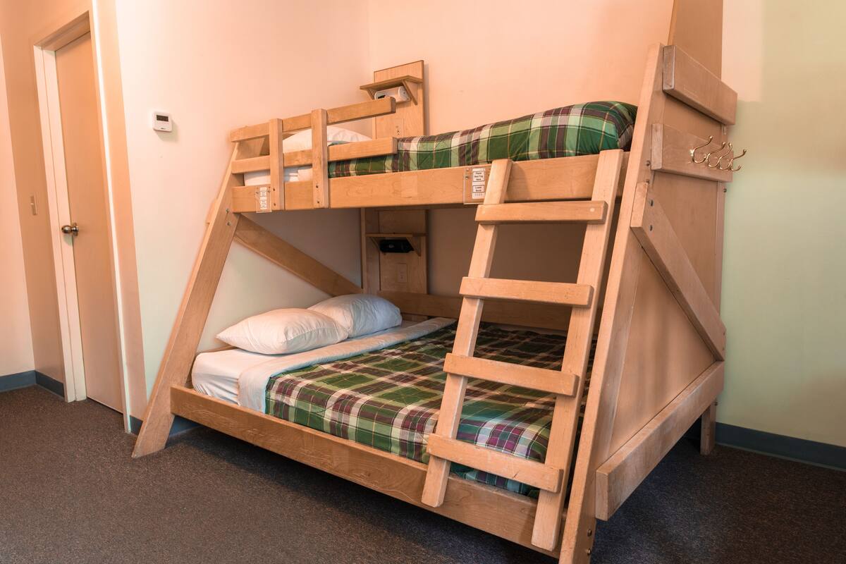 Un lit superposé avec une échelle, une petite étagère et un crochet fixé au mur.