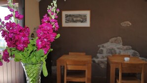 Una habitación con una mesa y sillas de madera, un florero con flores rosadas y un cuadro en la pared.