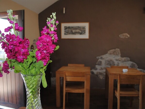 A room with a wooden table and chairs, a vase with pink flowers, and a framed picture on the wall.