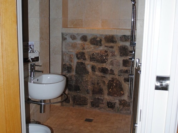 A bathroom with a stone wall, a white sink, and a shower. - Blas Gwyr (Swansea)