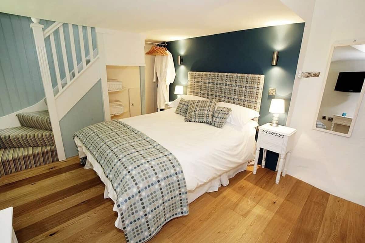 A bedroom with a bed, a nightstand, a TV, and a staircase.
