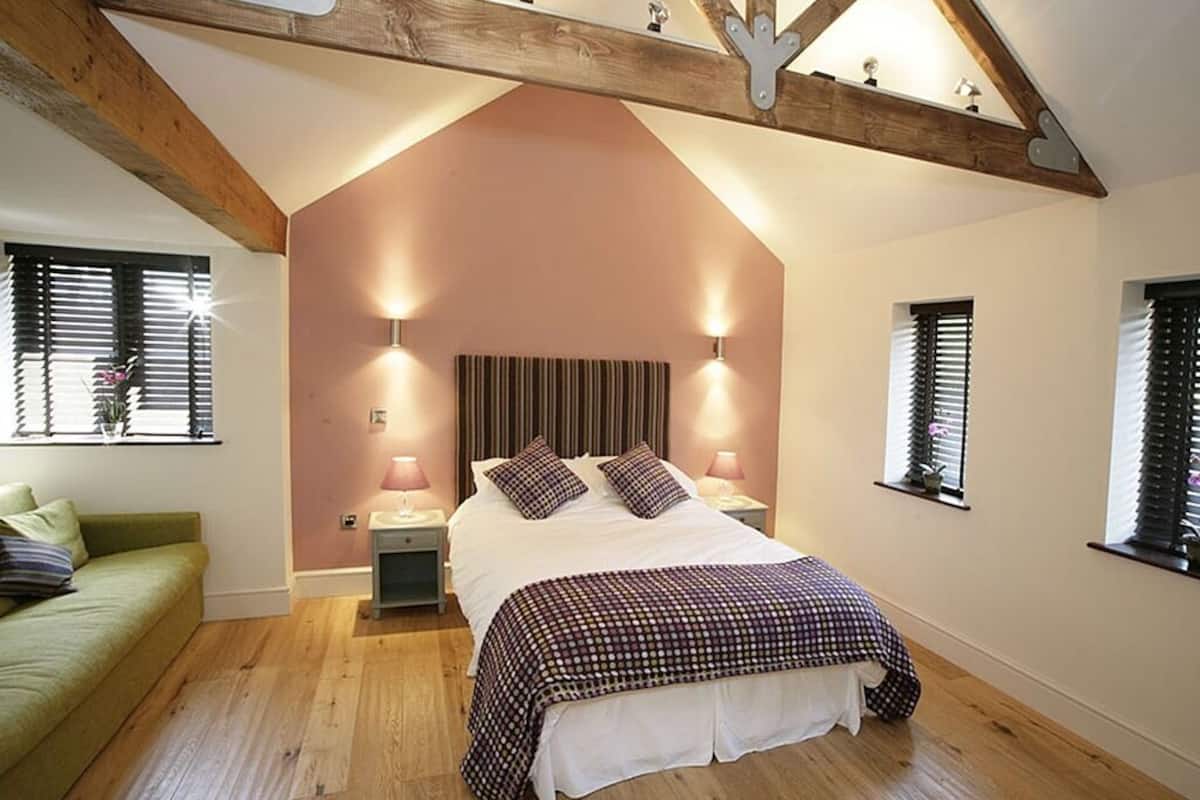 A bedroom with a sloped ceiling, a bed with a checkered bedspread, two bedside lamps, a nightstand, and a green sofa.
