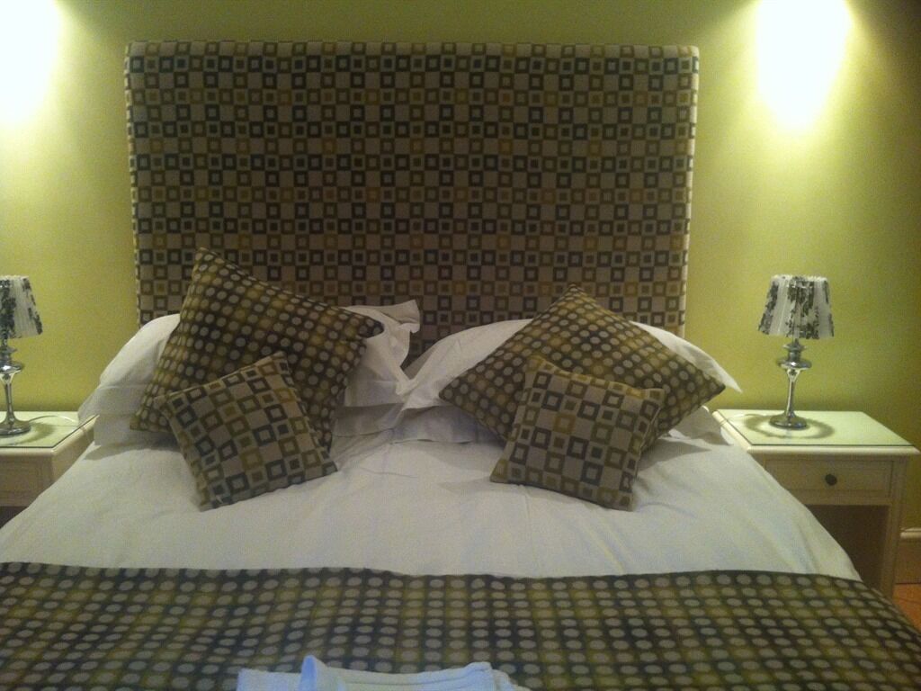 A bed with a patterned headboard, two bedside tables with lamps, and a patterned bedspread.