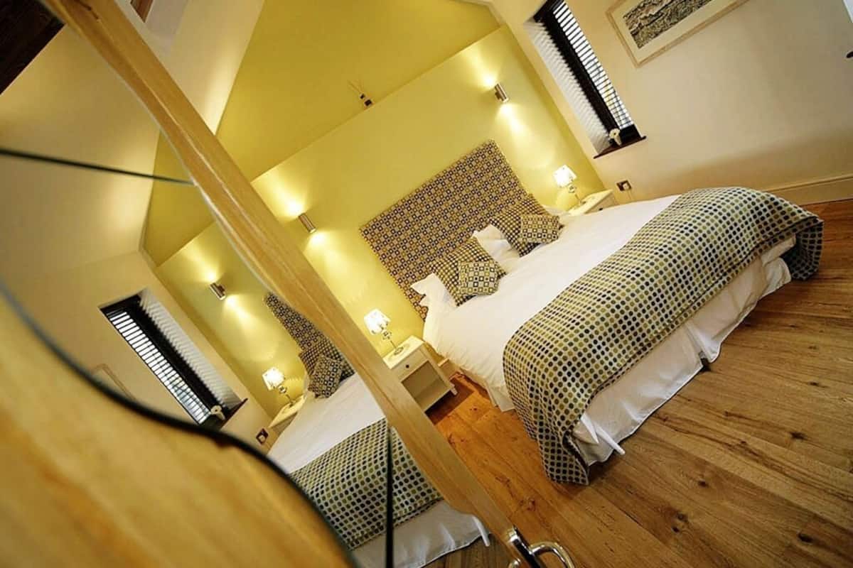 A bedroom with a large bed, a wooden floor, and a mirror reflecting the room.