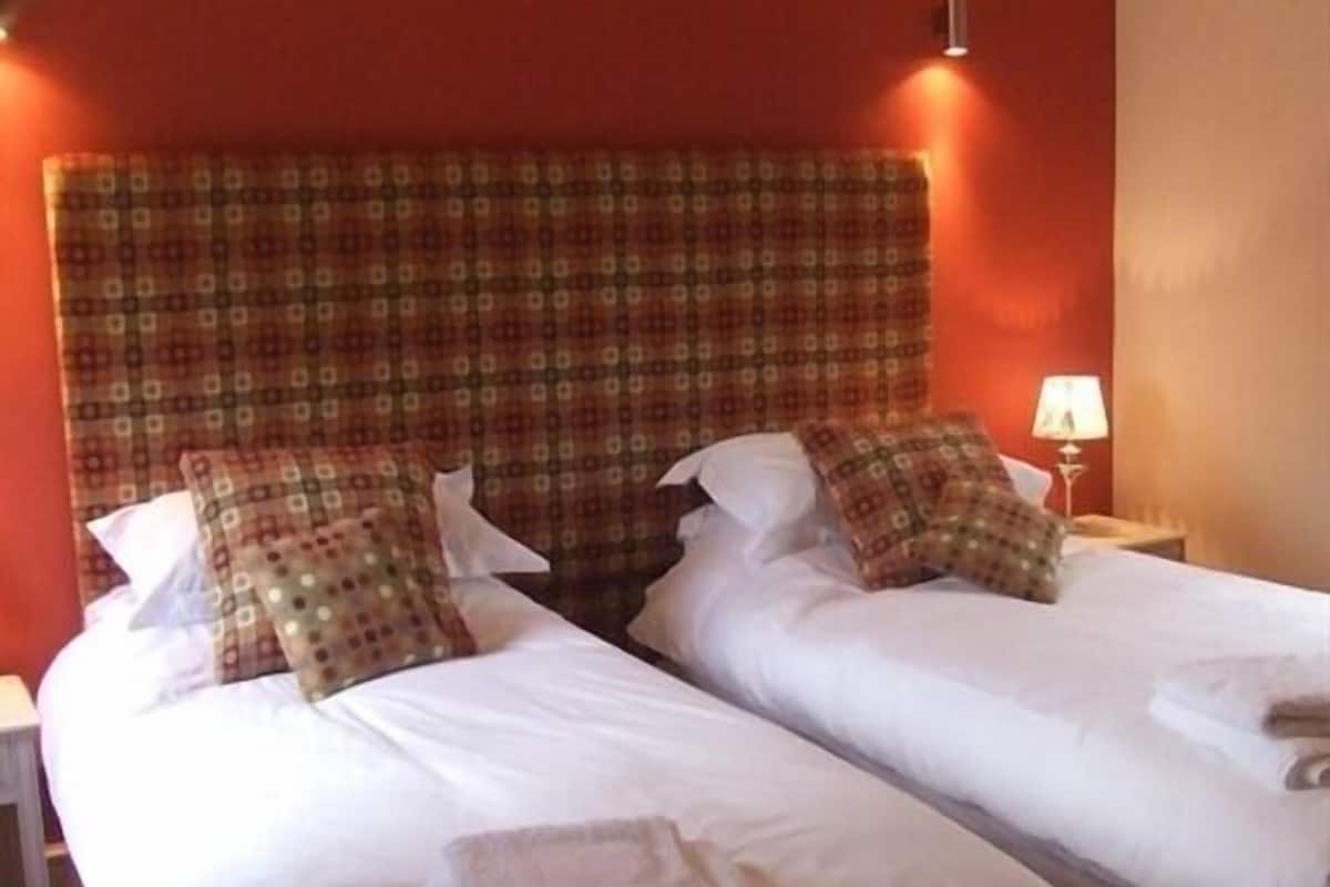 A hotel room with two beds, each with white linens and pillows, a patterned headboard, and a bedside lamp.