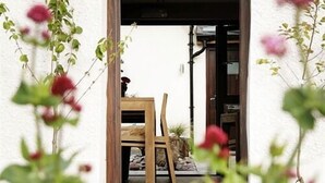 Un vano que da a una habitación con una mesa y sillas de madera, un muro de piedra y vistas al exterior.