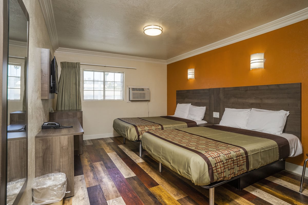 A hotel room with two beds, a desk, and a window.