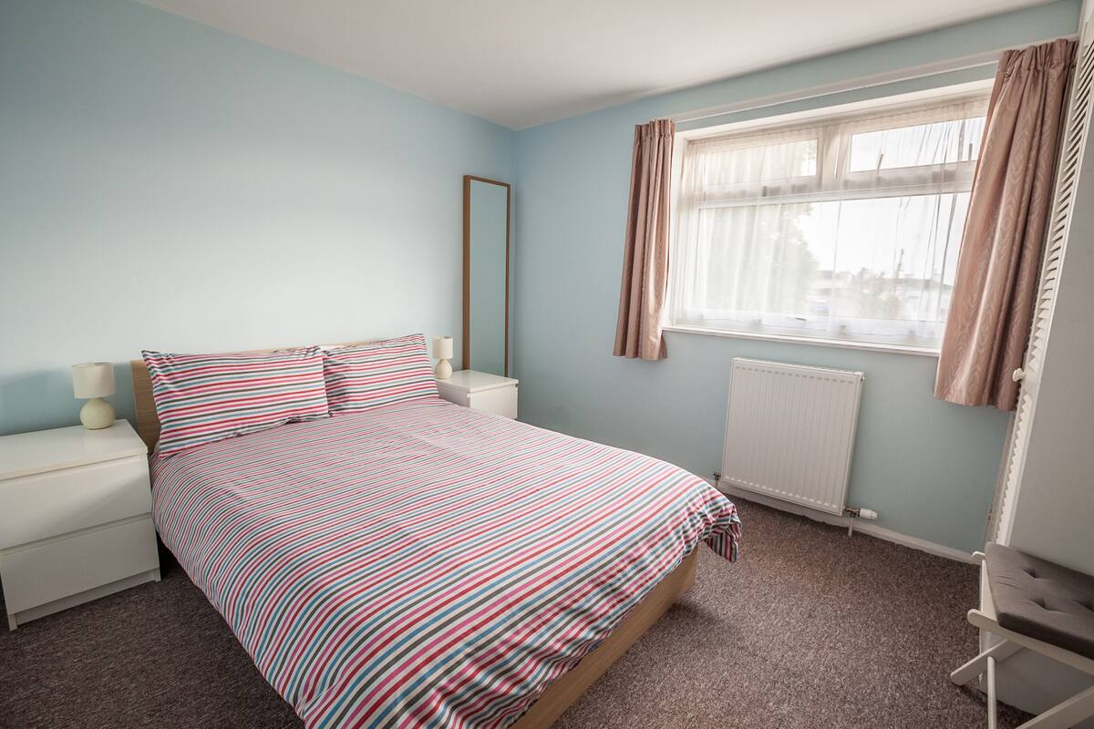 A bedroom with a bed, nightstands, a window with curtains, and a radiator.