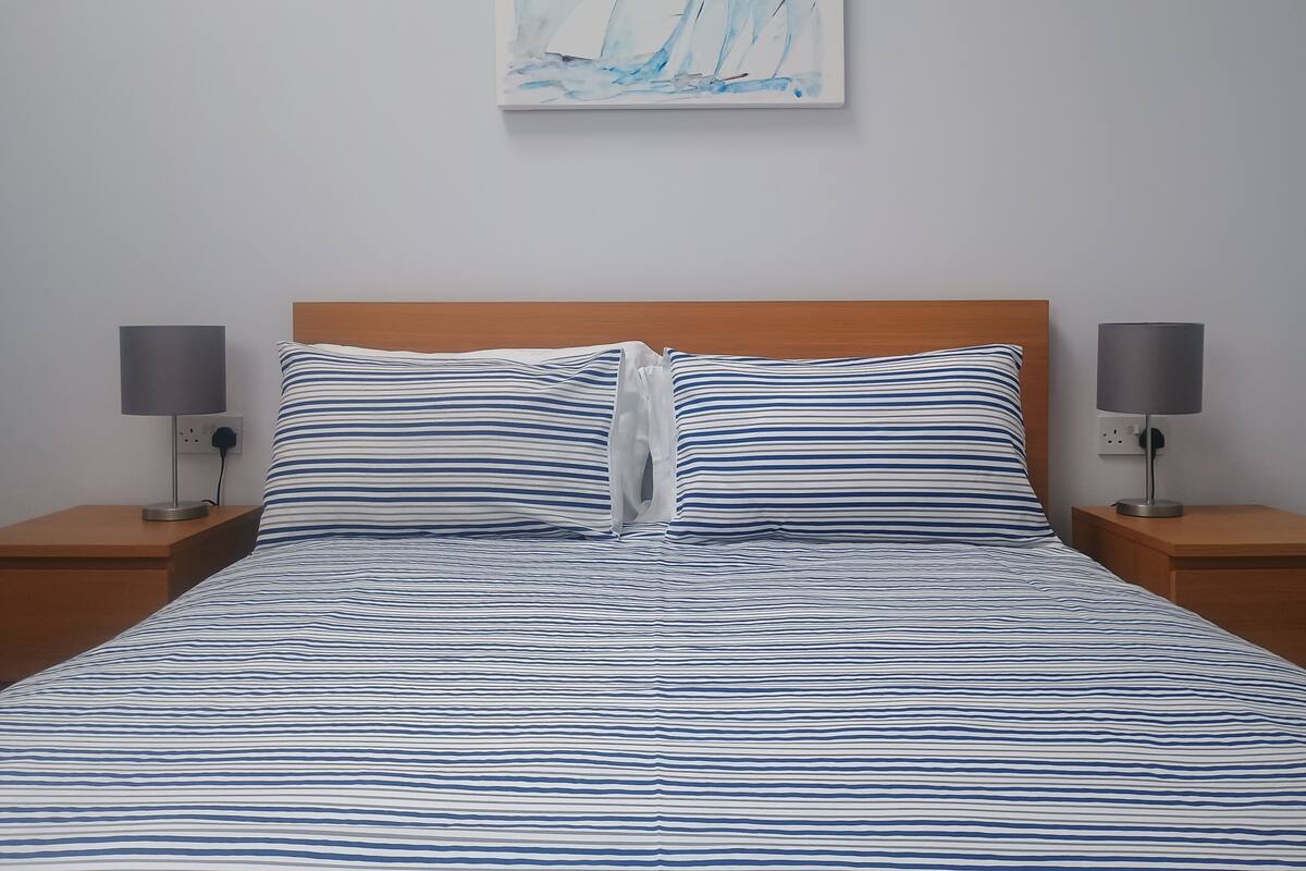 A neatly made bed with striped bedding, two bedside lamps, and a painting on the wall.