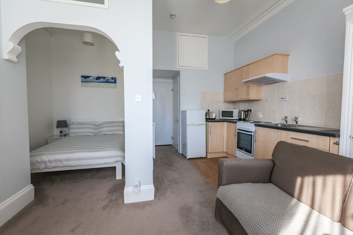 A compact living space with a bedroom, kitchenette, and a small seating area.