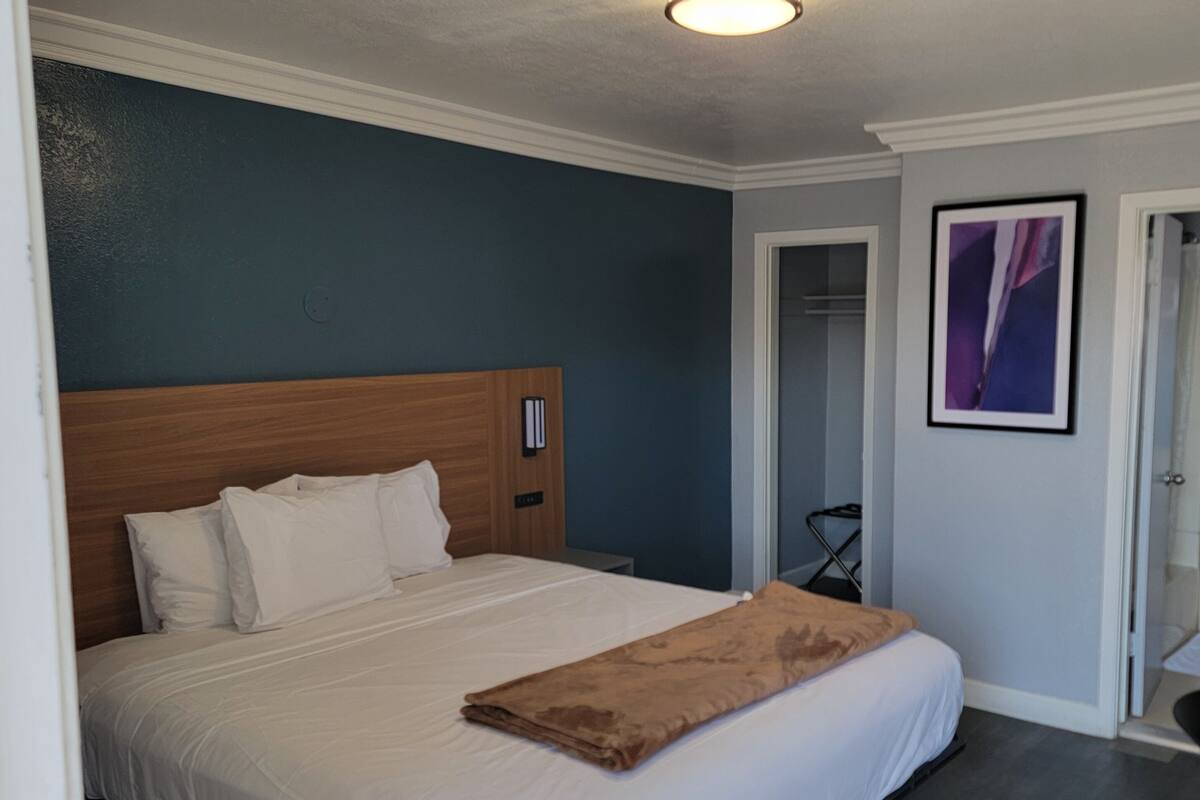 A hotel room with a bed, a wooden headboard, a white wall, and a door leading to a bathroom.