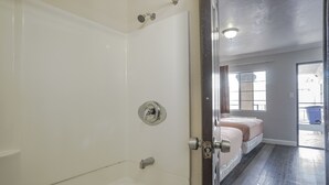 Un baño con bañera, ducha e inodoro. Hay una puerta que da a un dormitorio con cama y ventana.