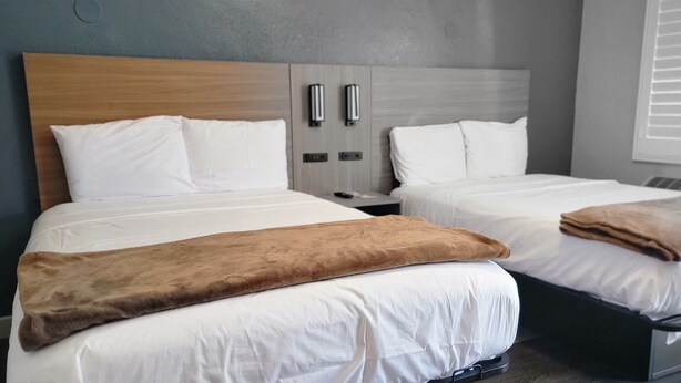 Una habitación de hotel con dos camas, cabecero de madera, mesitas de noche y una ventana con persianas.
