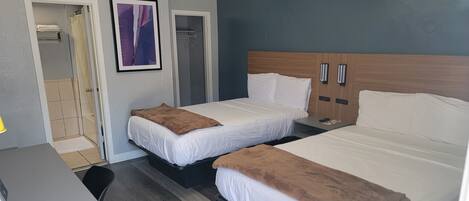 A hotel room with two beds, a wooden headboard, a small bedside table, and a shower area.