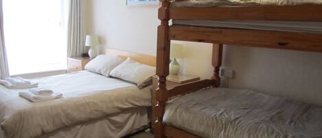 A hotel room with two beds, a window with curtains, a bedside table with a lamp, and a framed picture on the wall.