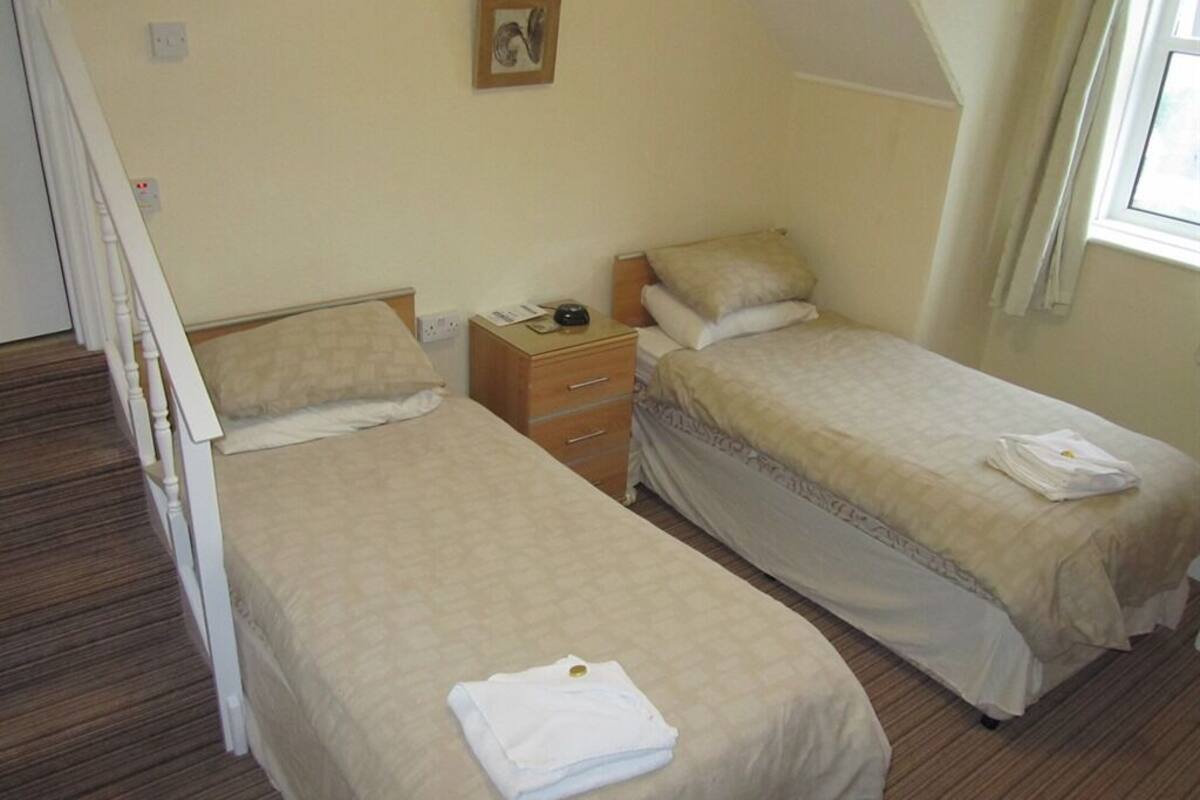Un dormitorio con dos camas individuales, una mesita de noche, un aparador y una ventana con cortinas.