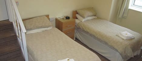A bedroom with two single beds, a nightstand, a dresser, and a window with curtains.
