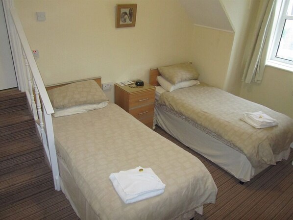 Un dormitorio con dos camas individuales, una mesita de noche, un aparador y una ventana con cortinas.