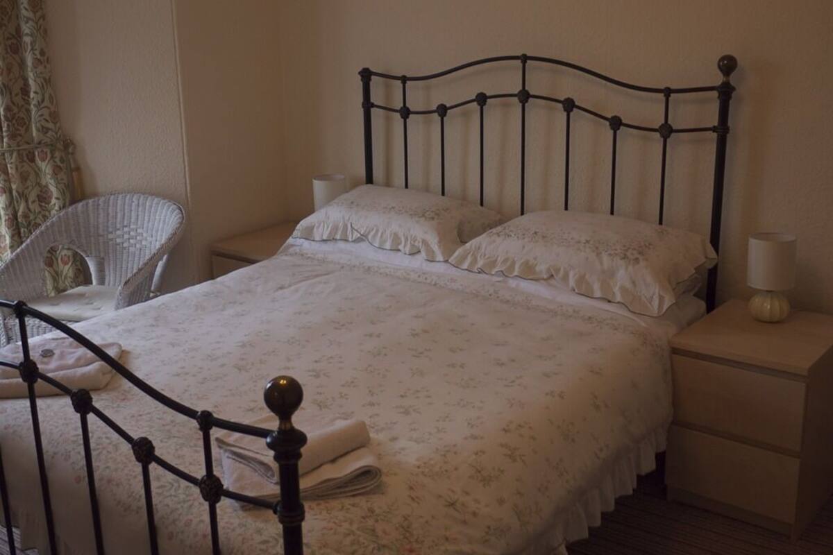 Una cama bien hecha con colcha floral, cabecera de metal y mesita de noche con lámpara.