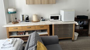 Una kitchenette compacta con microondas, tostadora y cafetera. Hay dos cuadros enmarcados en la pared, una lámpara y un mueble pequeño debajo de la encimera.