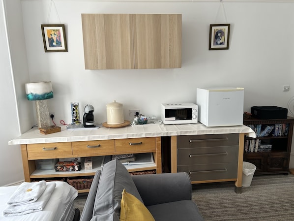 A compact kitchenette with a microwave, toaster, and coffee maker. There are two framed pictures on the wall, a lamp, and a small cabinet below the counter.