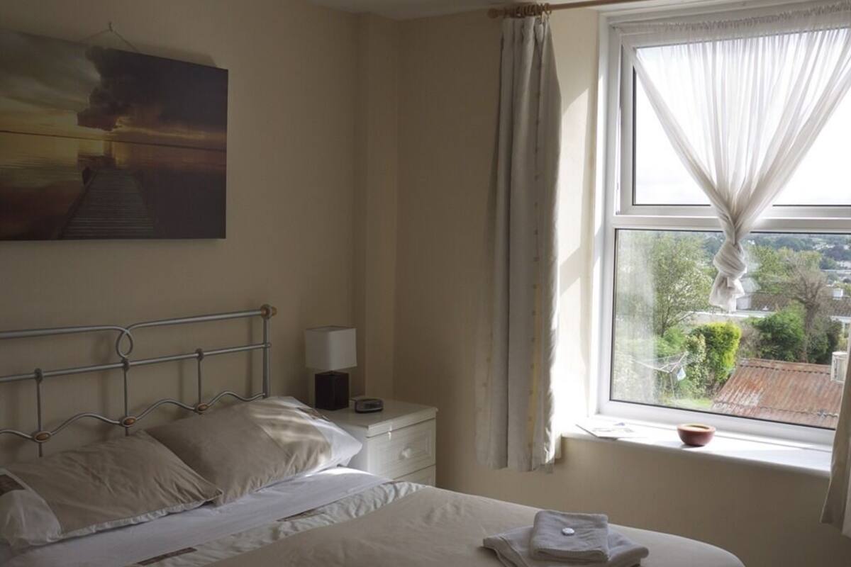 Un dormitorio con cama, mesita de noche, lámpara y ventana con cortinas.
