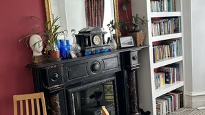 Una habitación con un escritorio de madera negra, un espejo grande, una estantería y una alfombra estampada.