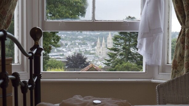 Un dormitorio con una cama, un ventanal con vistas a un paisaje urbano y una cortina.
