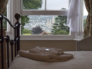 A bedroom with a bed, a window with a view of a cityscape, and a curtain.