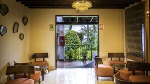 A hotel lobby with a tiled floor, wooden furniture, a chandelier, and a view of a tropical garden through a glass door. - Hotel Señorial (Lima)