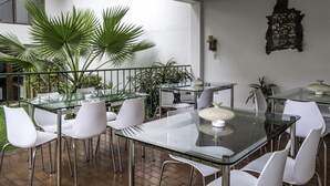 A modern dining area with glass tables and white chairs, surrounded by potted plants. - Hotel Señorial (Lima)