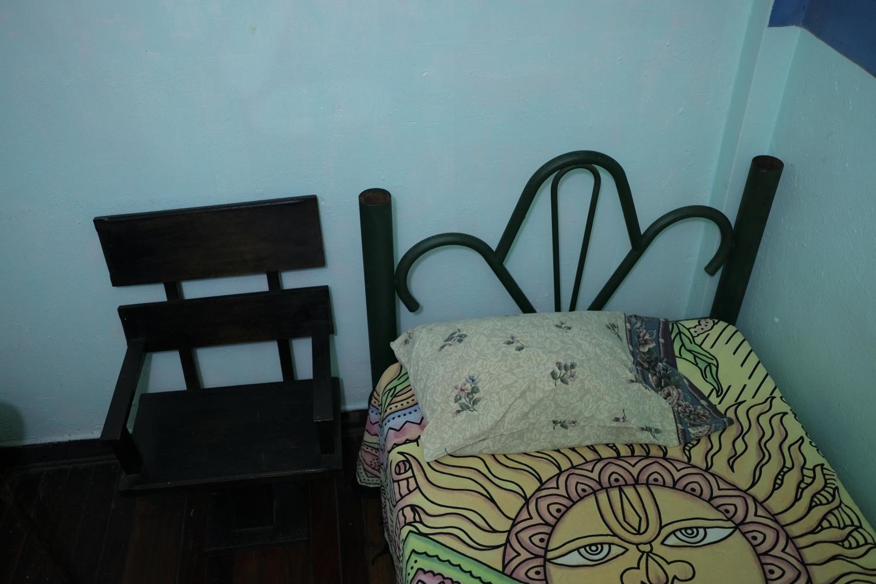 A room with a wooden bed frame, a chair, and a patterned bedspread.
