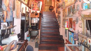 Una escalera estrecha con escalones de madera que conduce a una plataforma. Las paredes están decoradas con diversas obras de arte y máscaras.