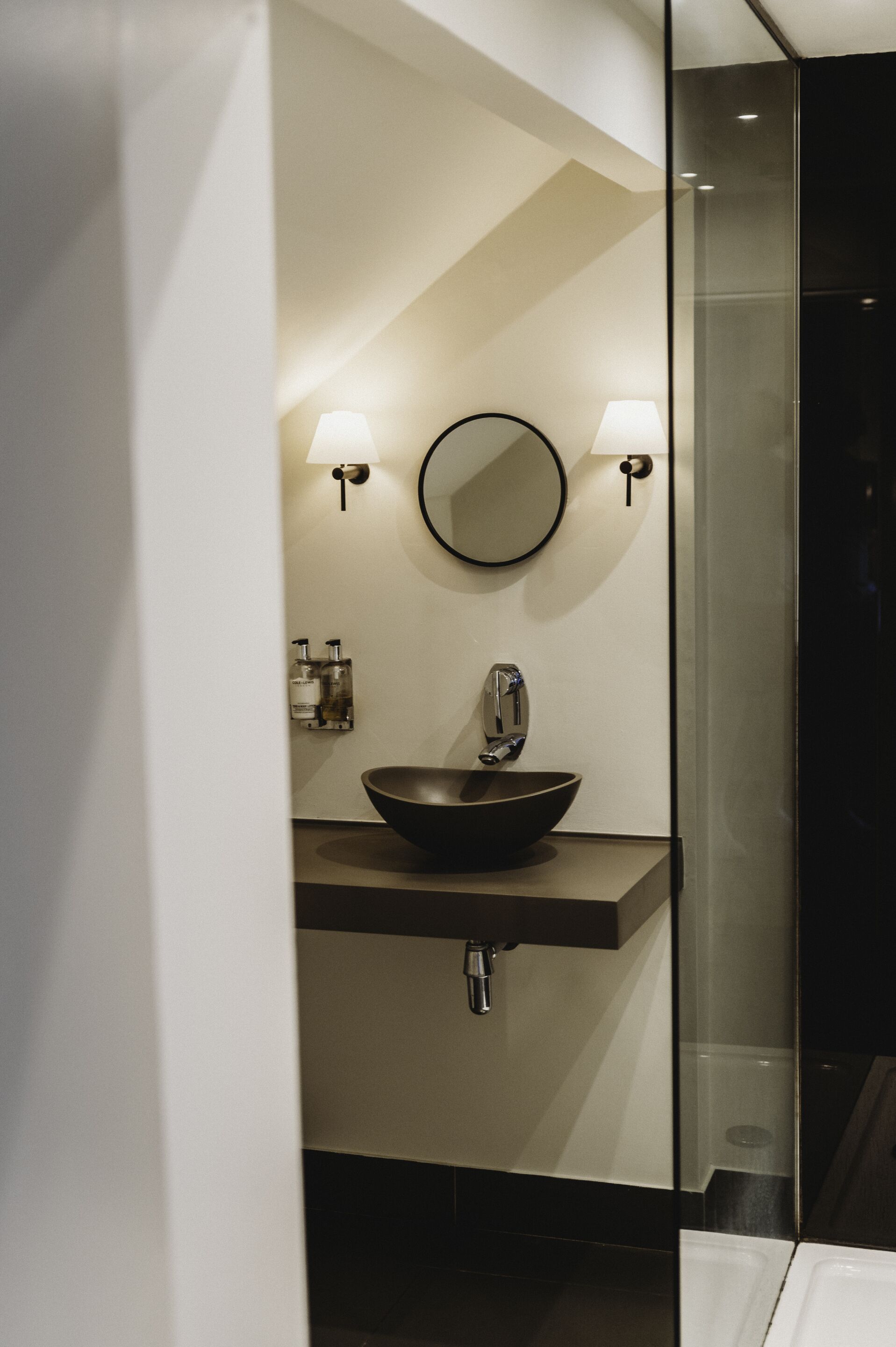 A modern bathroom with a black vessel sink, two wall-mounted lights, and a mirror.